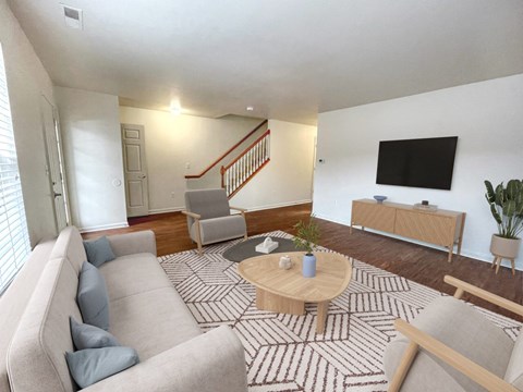 A living room with a grey couch, a wooden coffee table, and a TV on the wall.