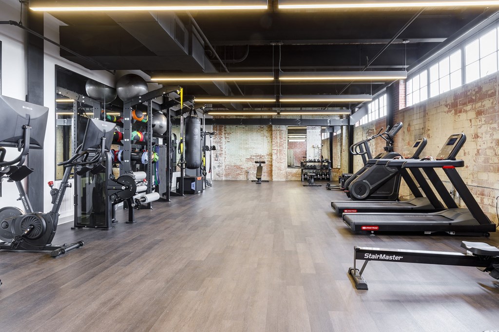 a gym with weights and cardio machines and a brick wall at The Mill at Prattville, Prattville, AL