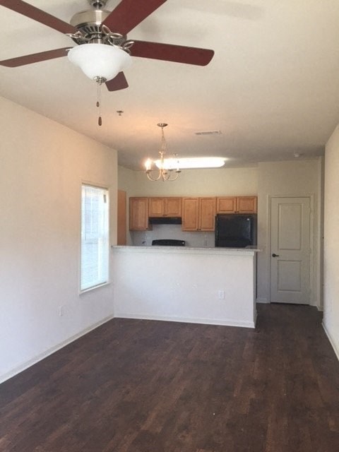 an empty living room with a kitchen and a ceiling fan