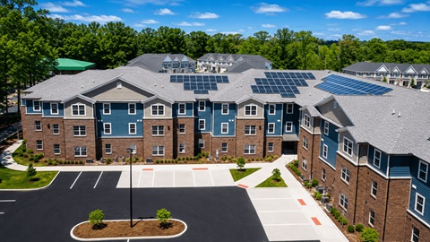 A large building with solar panels on the roof and a parking lot in front.