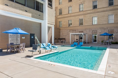 A pool with a blue umbrella and chairs around it.