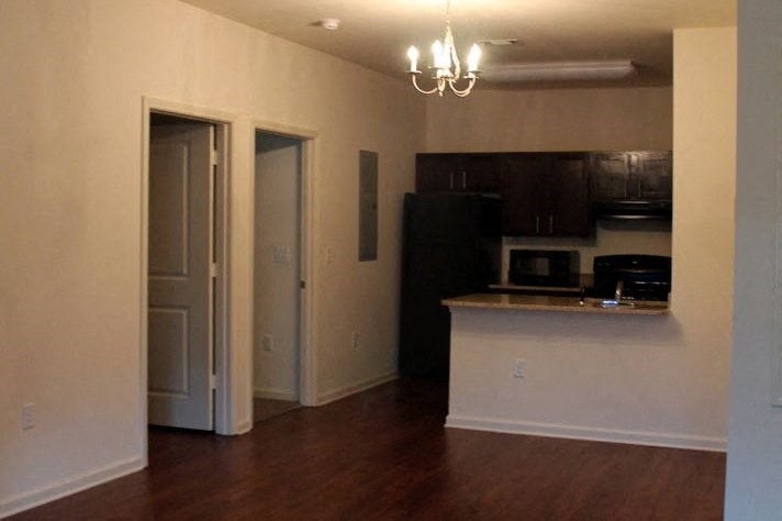 an empty living room with a kitchen and a door