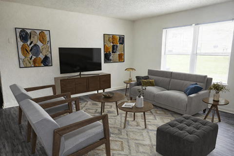 A living room with a grey couch, a wooden coffee table, a TV, and two chairs.
