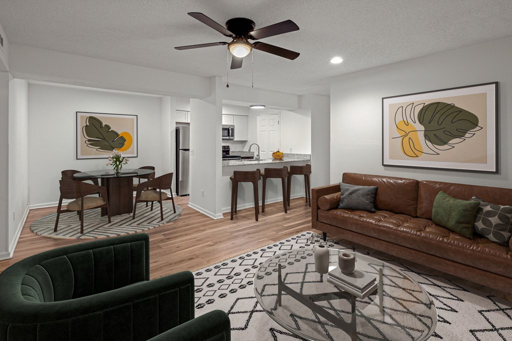 A living room with a brown couch, a dining table with chairs, and a ceiling fan.at Mammoth at the Orchard Apartments, Rogers, 72756  