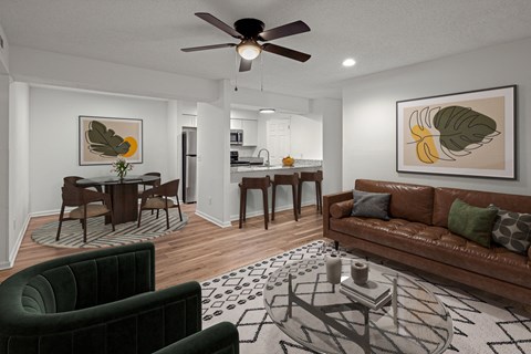 A living room with a brown couch, a dining table with chairs, and a ceiling fan.