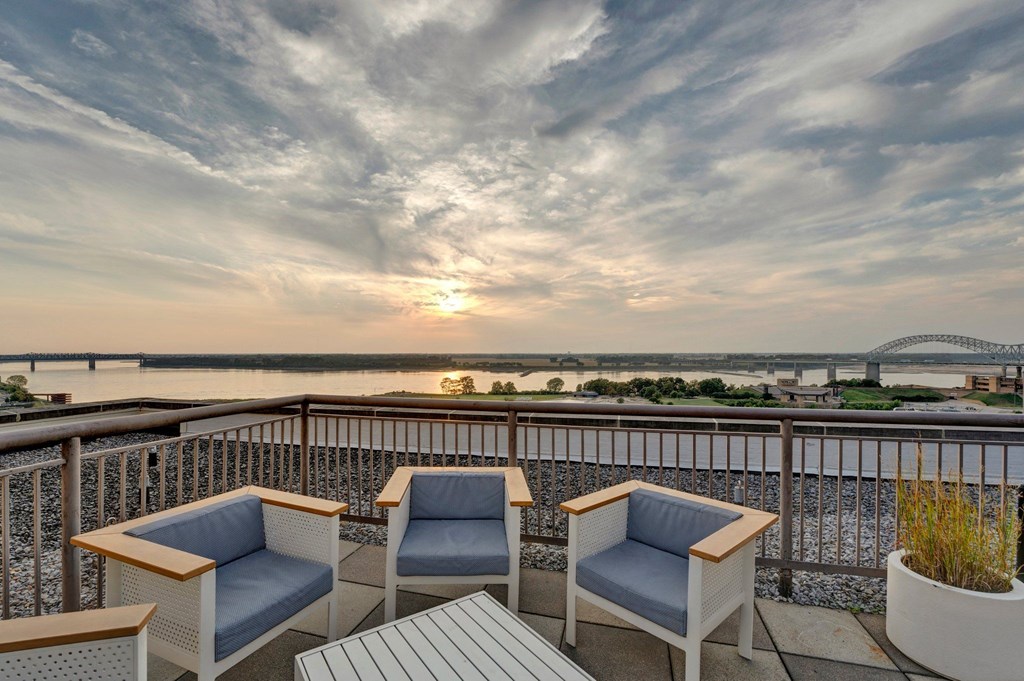 Two chairs and a table on a balcony overlooking a river at sunset.