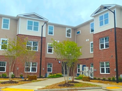 Apartment building with a mix of brick and siding exterior walls, surrounded by landscaping and a sidewalk.