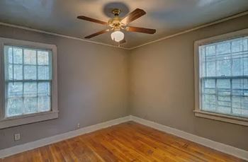 A room with a ceiling fan and two windows.
