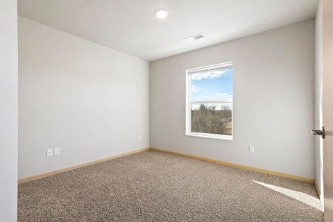 A room with a carpeted floor and a window showing a view of trees and sky.