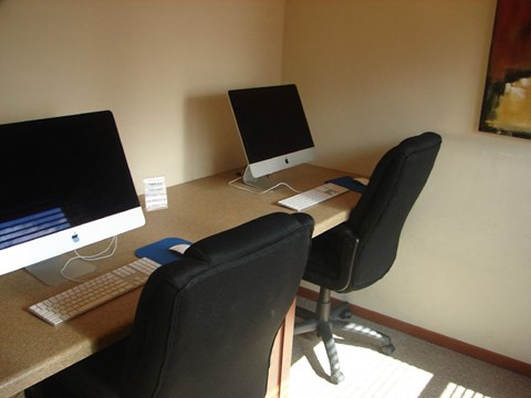 A black chair is in front of a desk with two monitors and a keyboard.