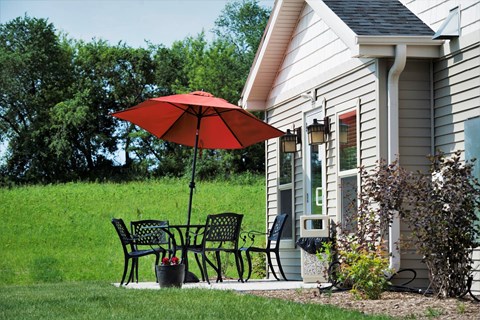 A red umbrella is on a patio table outside a house.