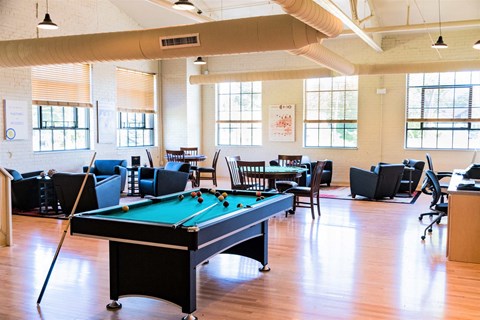A pool table is in the middle of a room with chairs and desks.