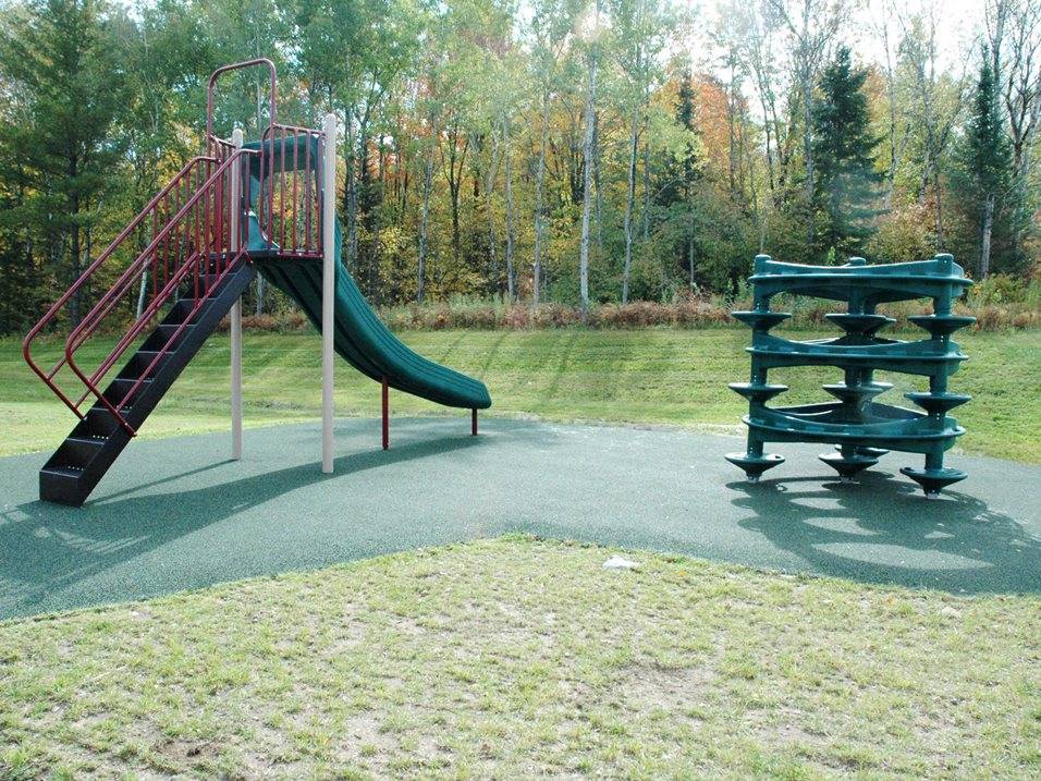 A playground with a green slide and a wooden bench.