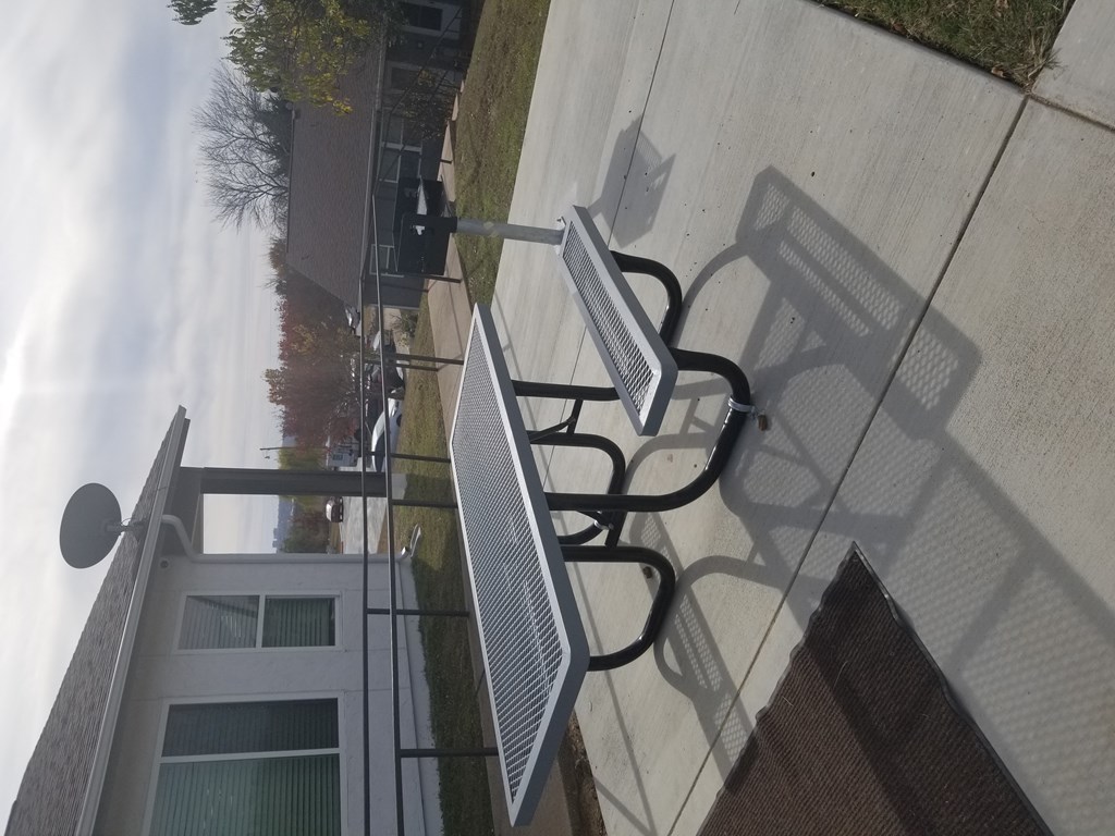 A metal bench with a backrest is on a sidewalk.