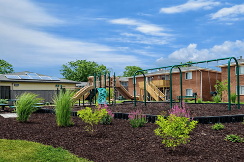 A playground with a slide and a green railing is in front of a building.