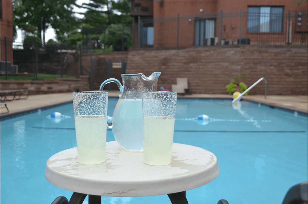 two glasses of lemonade on a table in front of a swimming pool