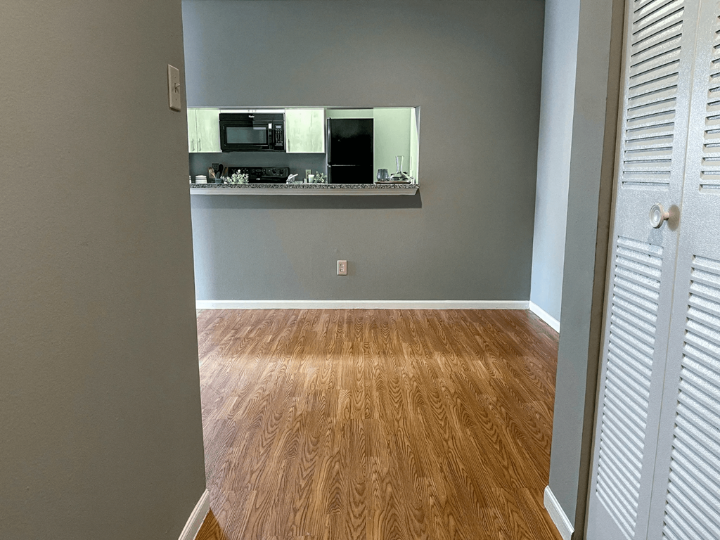 an empty room with a hard wood floor and a kitchen