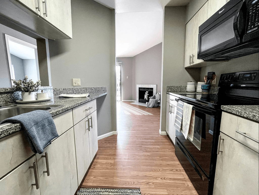 a kitchen with white cabinets and black appliances and a hallway with a fireplace