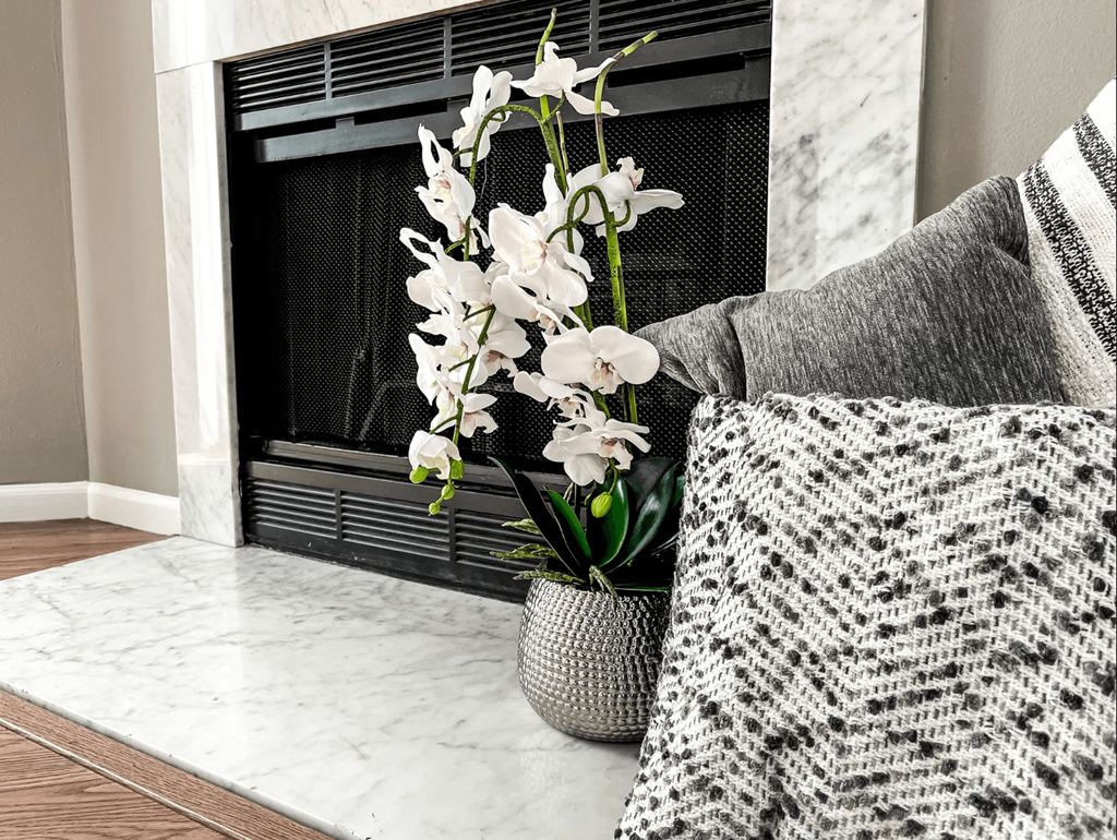 a vase with white flowers in front of a fireplace