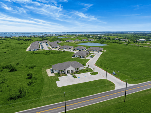A road with a sidewalk and a grassy area with houses in the background.