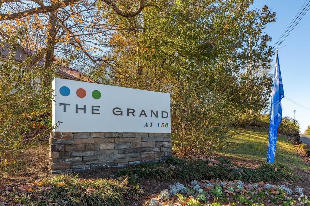 A sign that says "The Grand at 150" is in front of a tree.