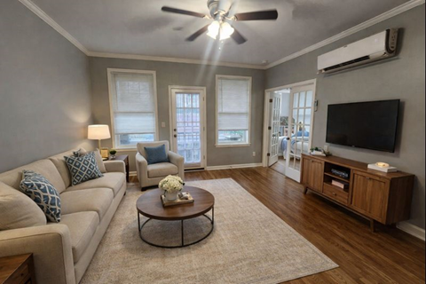 A living room with a beige couch, a coffee table, and a flat screen TV mounted on the wall.