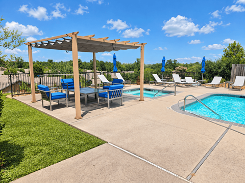 A pool area with a pergola and lounge chairs.