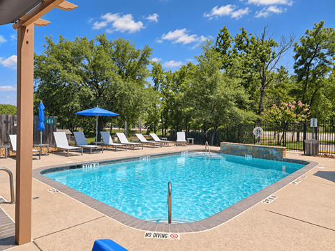 A pool surrounded by trees and chairs with a no diving sign.