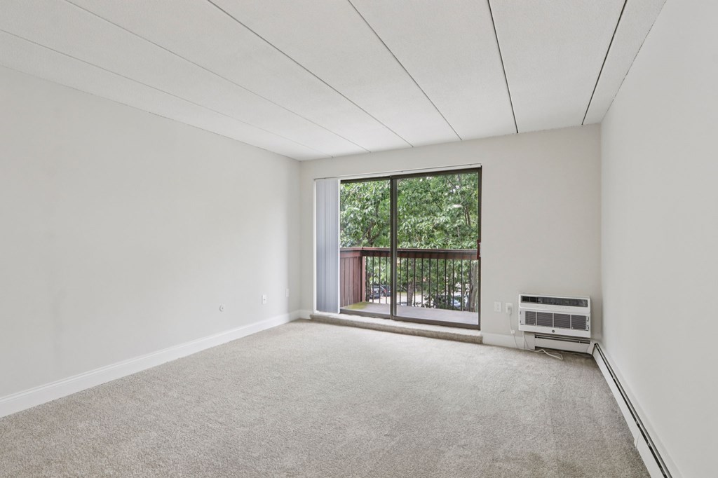 A room with a carpet floor and a window with a view of a balcony.