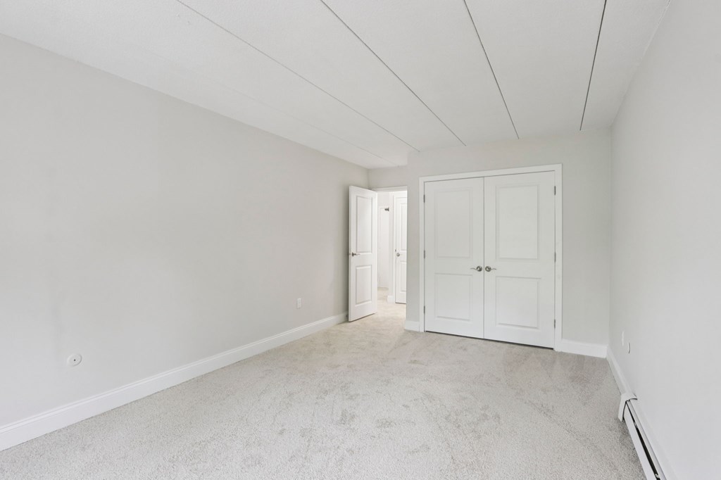 A room with white walls and carpeted floor with two doors.
