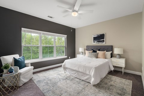 A bedroom with a large bed, a window with a view of trees, and a ceiling fan.