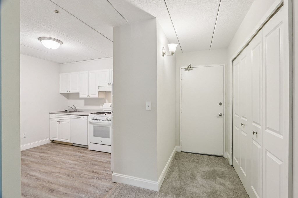 A kitchen with white cabinets and appliances in a room with a carpeted floor.