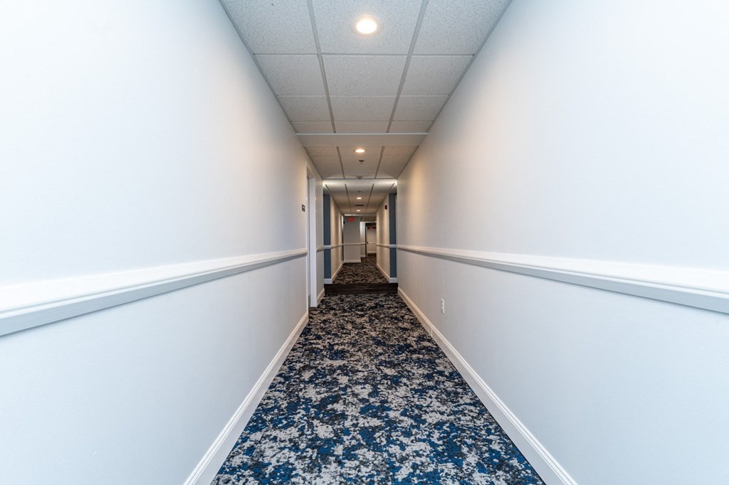 a long corridor with white walls and blue carpet