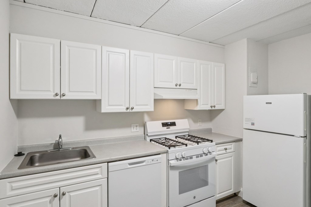 A white kitchen with a stove, sink, and cabinets.