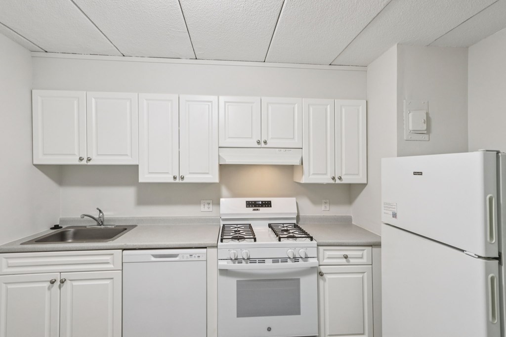 A white kitchen with a stove, sink, and refrigerator.