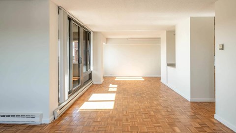 Long living area with parquet flooring, large sliding windows, and bright natural light entering from the balcony side.