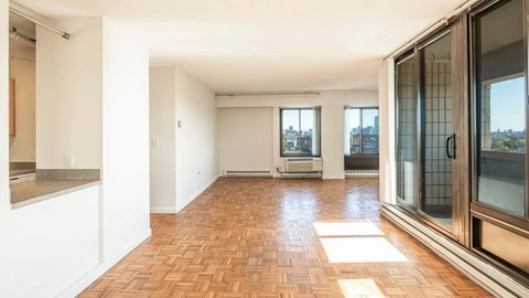 Spacious living room with parquet floors, wide windows, and ample natural light extending across the open layout.