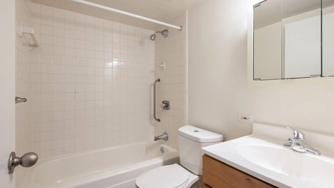 Bathroom featuring a tiled shower-tub combination, white fixtures, and a wood vanity.