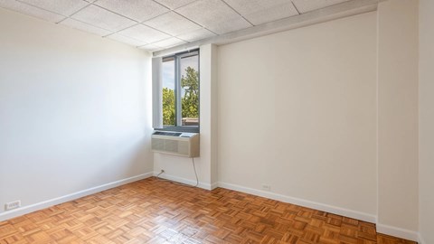 Bright bedroom with parquet flooring, a large window, and built-in air conditioning.