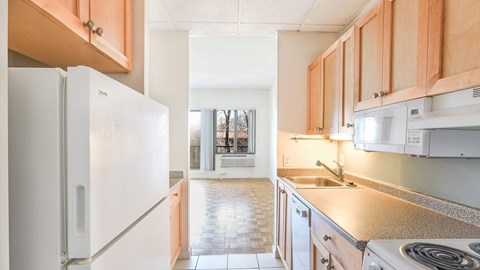 Galley kitchen with maple cabinets and view into bright living area with parquet flooring at 929 Mass Apartments in Cambridge MA.