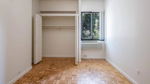 Bedroom with parquet flooring, open closet, and window overlooking greenery at 929 Mass Apartments.