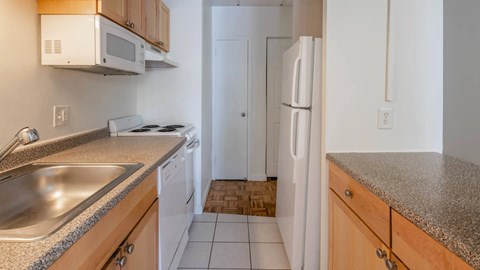 Galley kitchen with speckled countertops, white appliances, and wood cabinetry at 929 Mass Apartments.