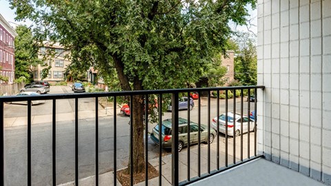 Private balcony view overlooking a residential street with trees and parked cars at 929 Mass Apartments.