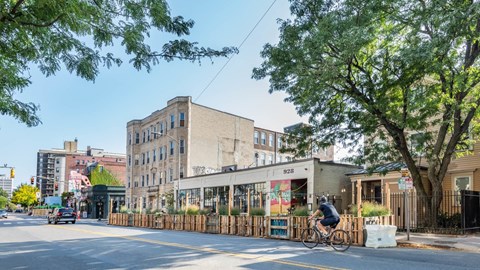 Street view with cyclist passing outdoor dining and neighborhood shops near 929 Mass Apartments in Cambridge MA