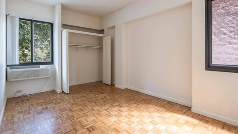 Bedroom with parquet flooring, open closet, and window overlooking greenery at 929 Mass Apartments in Cambridge MA