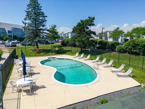 A large swimming pool surrounded by lawn chairs and trees.