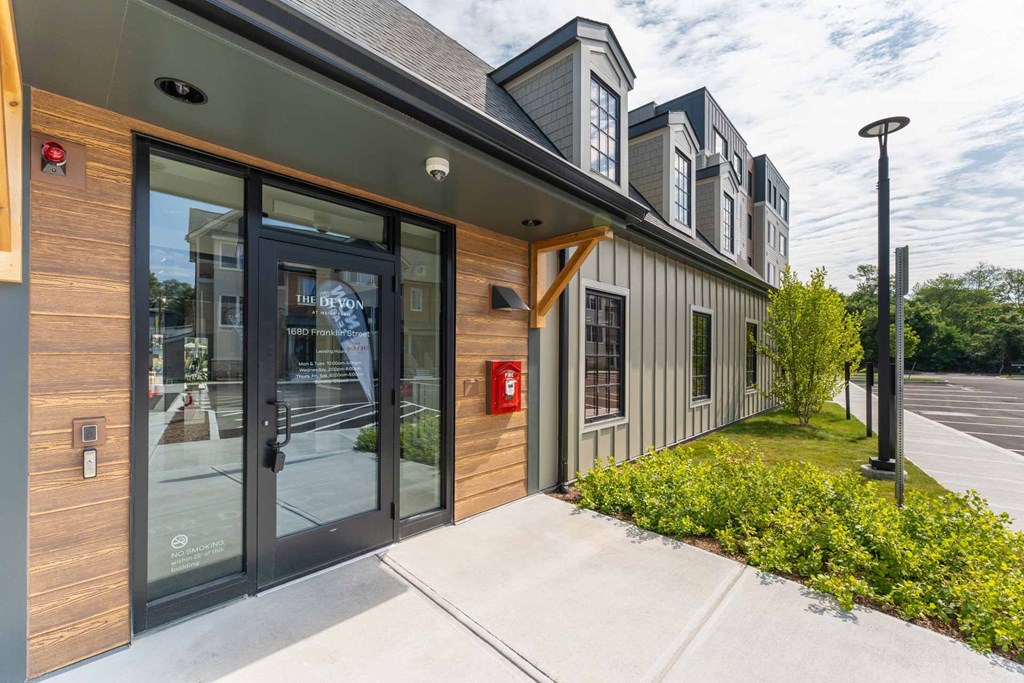 Leasing office entrance at The Devon at Weiss Farm apartments in Stoneham, MA with glass door and landscaped pathway.