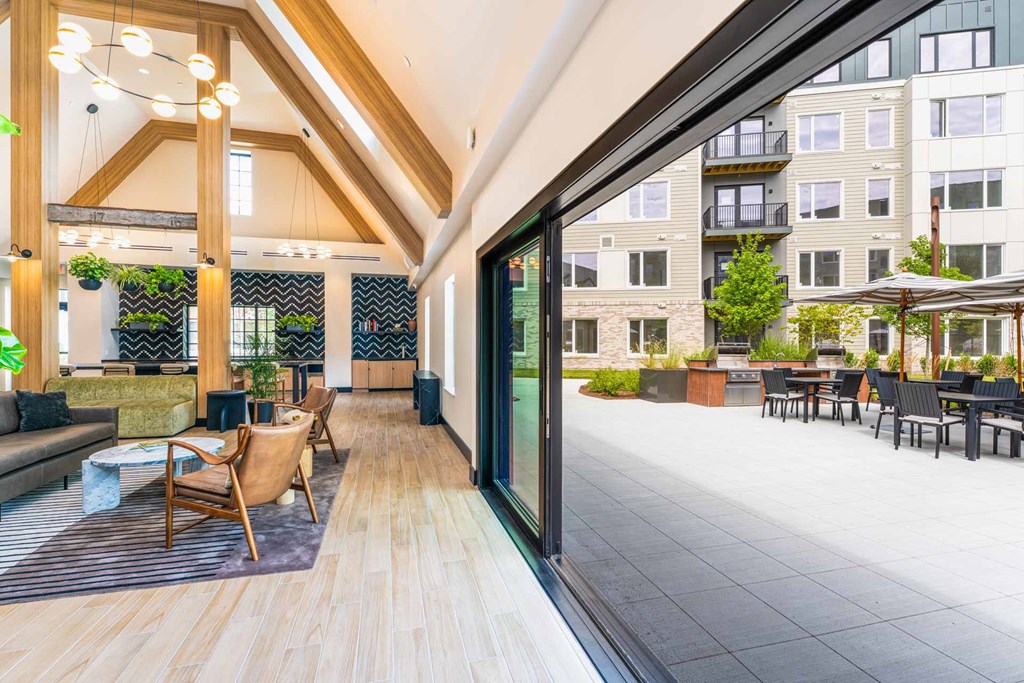 Lounge opening to outdoor patio with grills and seating at The Devon at Weiss Farm apartments in Stoneham, MA.