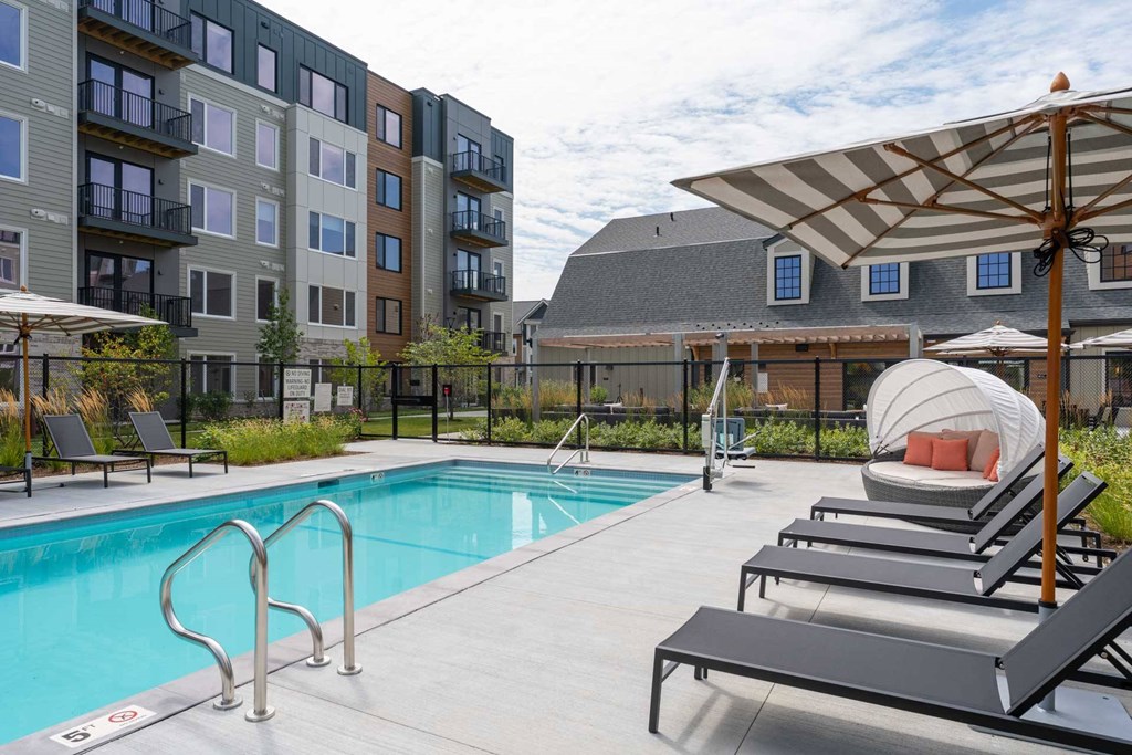 Pool area with sun loungers, striped umbrellas and cabana at The Devon at Weiss Farm in Stoneham, MA.