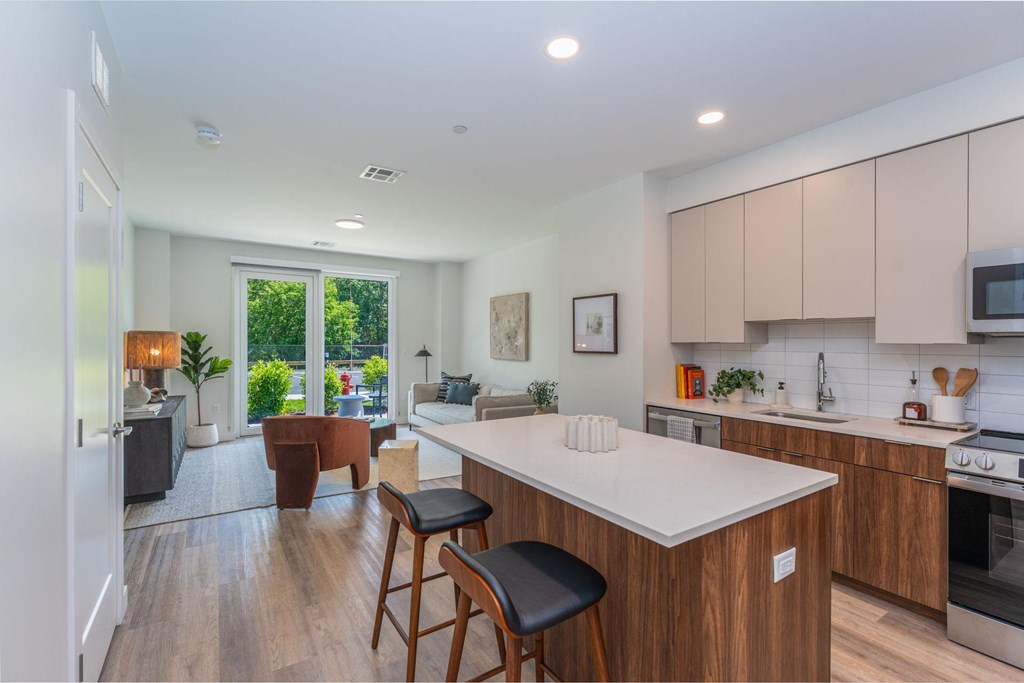 Modern kitchen and living room with quartz island and stainless appliances at The Devon at Weiss Farm in Stoneham, MA.